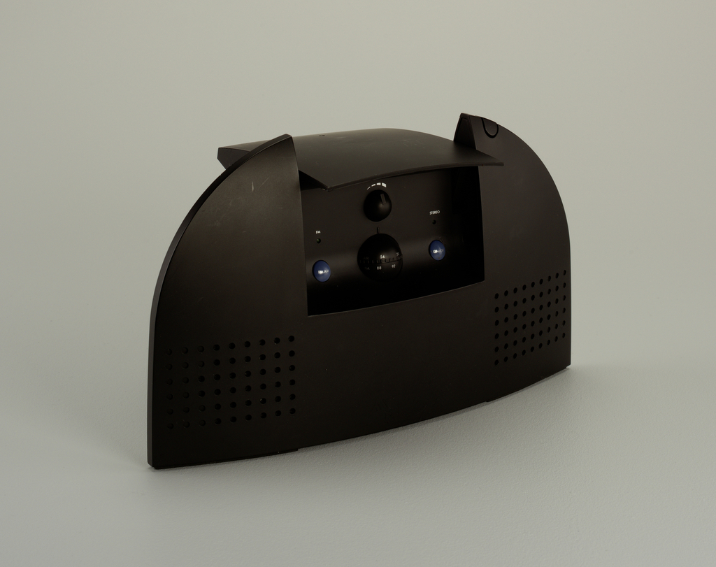 Here we have a sleek, all black radio. It has a rectangular base that curves into a long, ovoid arc at the top. Width-wise, it is extremely thin. The front has two speakers on the left and right made of a square grid of dots near the bottom of the radio. There is a window-like opening in the center of the radio to reveal a minimal console with controls. The console has four spherical buttons: the center, largest button is the AM/FM tuner. To the left and right are smaller blue buttons, and above the tuner is the volume adjustment. To the right of the window opening is a button that runs along the top of the arc.