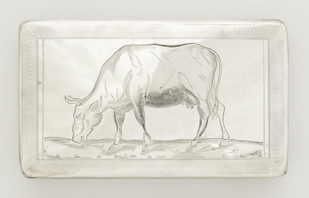 Top view of a rectangular silver box with rounded corners and a flat lid, engraved with a wavy border around a grazing cow. The cow faces left, head bent to the irregular line of the ground; its tongue appears to lick the short grass. The cow has short curvy horns, a bulky body, and slender legs. It is shaded with curving engraved lines and crosshatch. The frame around the cow is wavy lines in a scalloped pattern.