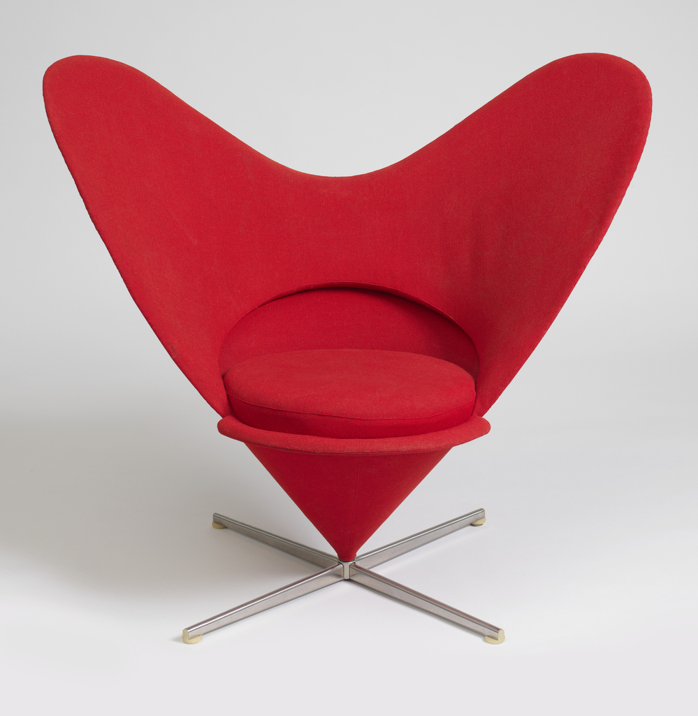 A concaved heart-shape chair upholstered in bright, cherry-red woven wool. A roung cushion of the same color and material rests on the seat. The wings of the chair form an inverted cone shape meeting at the horizontal x-form steel base on which it is mounted.