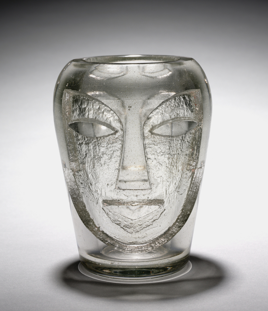 Vase of acid-etched glass. The design shows a face with almond-shaped eyes and is a visual reference to African masks. The face is somewhat pebbled, but the eyes, forehead and nose have not been etched.