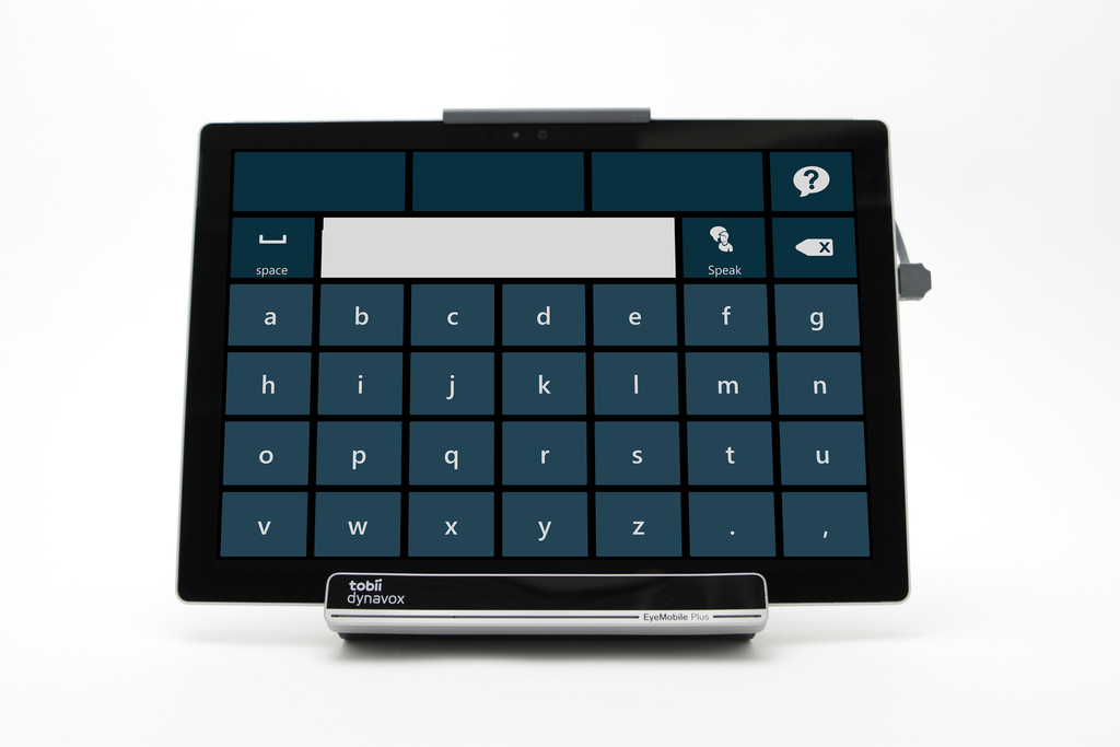 Tablet with built in keyboard. The tablet is placed on a handsfree metal stand. The tablet has six rows in total. On the top row are three long space bars keys and one key with a symbol of a talk bubble icon and a question mark in the middle. On the second row is button that says 'space' and next to it is a long white blank rectangular key. Then there is a key with a person and a talk icon above their head with the words 'Speak' below. The last key on the row is a space key. On the third row below are seven keys with the letters 'a, b, c, d, e, f, g'. On the forth row below are seven keys with the letters 'h, i, j, k, l, m, n'. On the fifth row below are seven keys with the letters 'o, p, q, r, s, t, u'. The last row has seven keys with the letters 'v, w, x, y, z.' The last two keys are of a period and then comma.