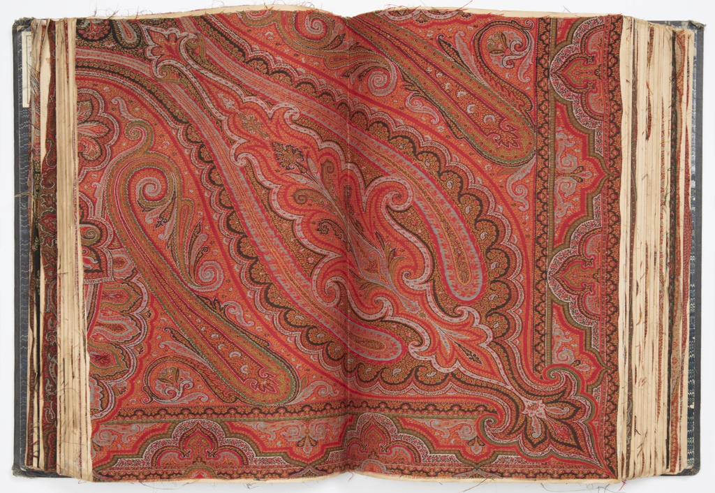 A large, teardrop-shaped pattern extens from the top left of the book to the bottom right. In the pattern are many smaller patterns, each resembling a floral shape. The colors are mostly in the range of pinks, oranges, and reds. On either side of this pattern are two smaller shapes, resembling candy-canes, with green borders and red/pink/orange insides.