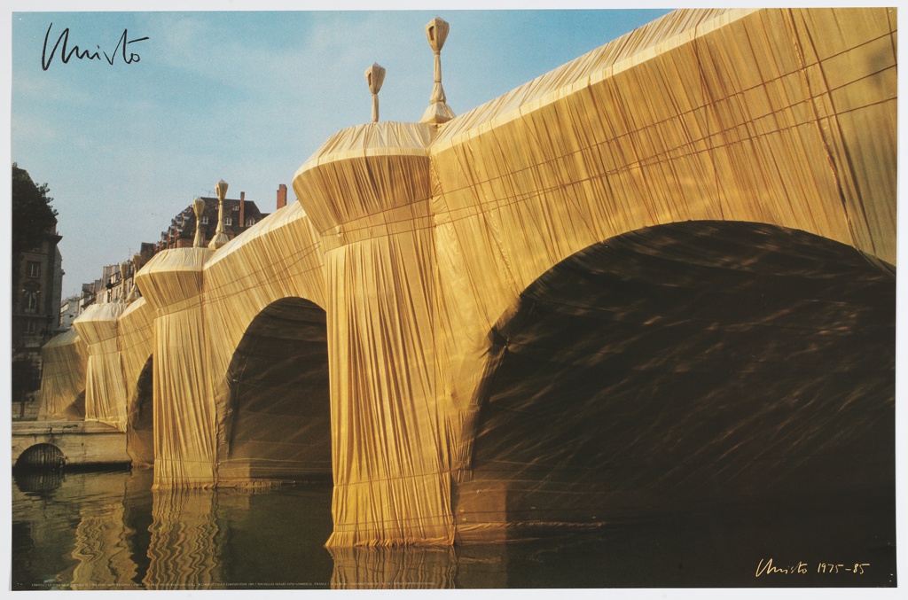 Photograph of Christo's land art project The Pont Neuf Wrapped. It has the Pont Neuf bridge on a sunny day, picture taken from the water. The bridge's facade is completely covered in yellow fabric with traces of rope securing the gold folds. The fabric covers the bridge entirely, including the lightposts on top. It is signed and dated by Christo.