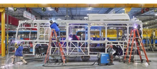 Photograph, Welders adding parts to the steel frame of an electric public transit bus