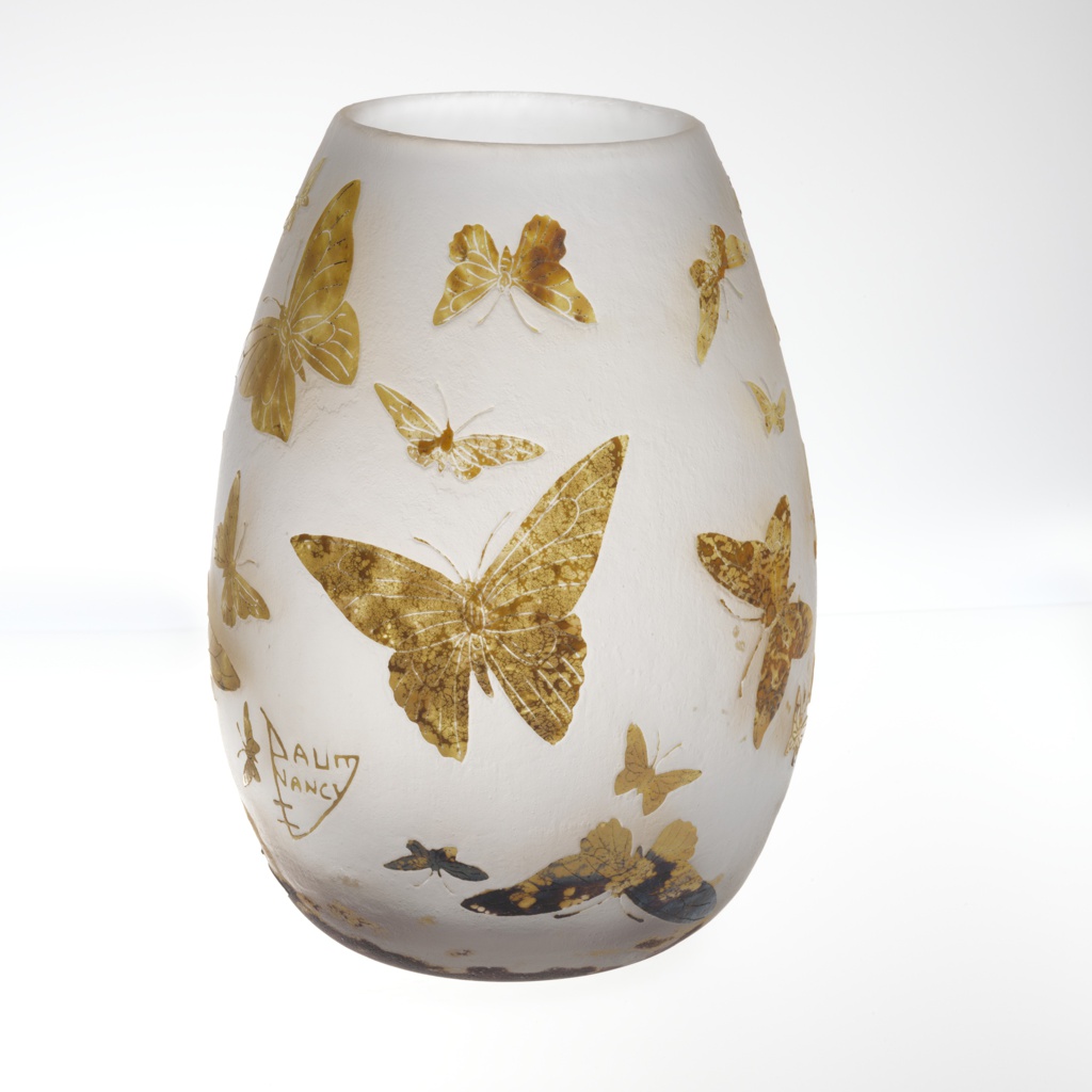 A bulbous vase with various yellow-brown butterflies scattered over the white glass. The mottled butterflies are a mix of sizes and shapes and face up, down, and sideways, with details etched in simple lines. At the lower left of the vase is a marking reading 'Daum / Nancy' in a conjoined triangular shape, with the strokes of D and N meeting those of M and Y in a point below the words.