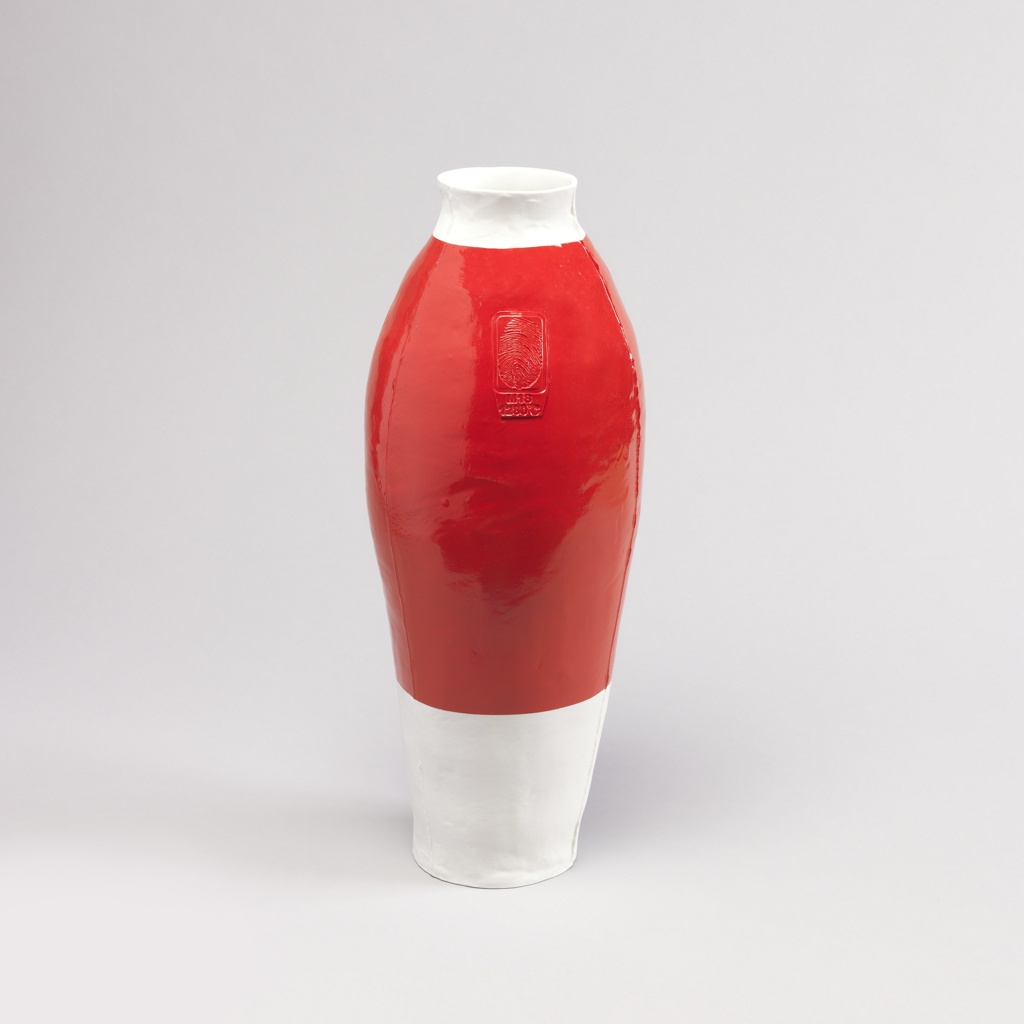 A white porcelain body ovoid form with circular mouth vase. Middle of the body is covered in bright red automotive paint. A raised rectangle lies at the shoulder of the vase, enclosed is an oversize thumbprint with 'M18,' 1280°C' below.