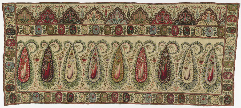 A horizontal rectangular shawl border featuring a row of nine large paisley cones on beige ground. The colors within the cones rotate between red, black, beige, light blue, and yellow green. Each contain a small floral border in a contrasting color with a central bouquet with four flowers. Each cone is surrounded by thin green leaves creating a fur-like border that crosses at top and curls to either side. A broad guard borders four sides around the central cones and extends up to top of shawl. Border creates a wide H shape that is connected at bottom. The border consists of octagonal medallions, each framing a floral spray in shades of green, red, black, and light blue, with oak leaves between. Broad border at the top with a row of decorated scalloped mounds with flowery sprays growing on and in them. Small cypress shape in center of each and between each mound. Thin zigzagged lines in pink, brown, and green define each section.